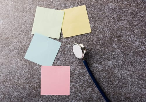 Above blank paper stick note list yellow, green, pink and blue with doctor stethoscope on concrete background, Health reminder concept