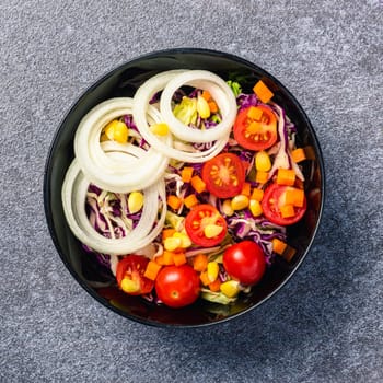 Top view of the healthy colorful salad bowl with tomatoes fresh mixed leaves vegetable in a dish on cement stone table background, Health salad snack diet food weight loss concept