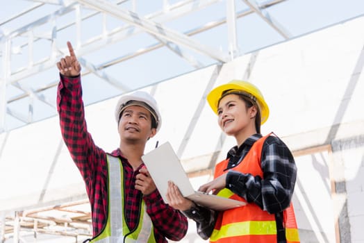Asian engineer foreman worker man and woman working at building construction site use laptop and talking with radio, engineering hold computer and radio discuss and control worker employee to building