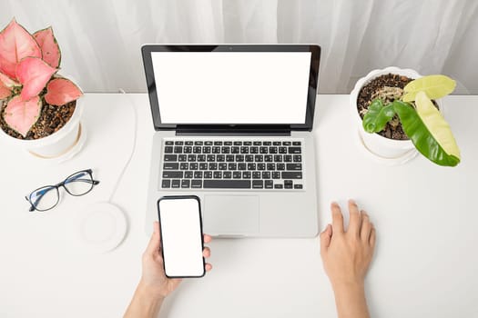 Female sitting workspace using hand holding black smartphone blank screen mock up on a table with laptop computer, female hold mobile phone with notebook at office