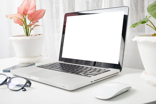 Modern workspace, mock up laptop computer blank white screen, eyeglasses and smartphone white table have potted plants on the desk, Notebook and mobile phone on desktop home office