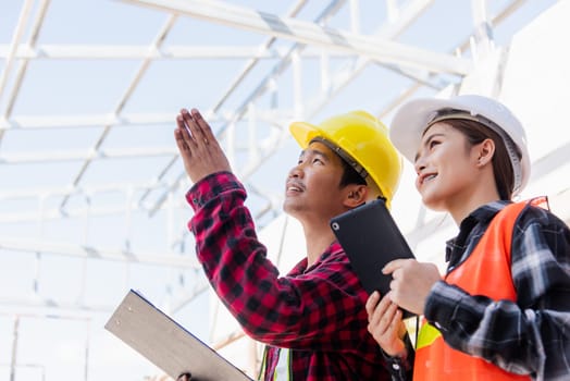 Asian engineer foreman worker man and woman working at building construction site use tablet talking to checking, engineering hold clipboard and discuss and control worker employee to building