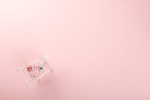 Shopping cart with vaccine vials bottles and syringes for vaccination against coronavirus, medicine illness, COVID-19 disease vaccine isolated on pink background