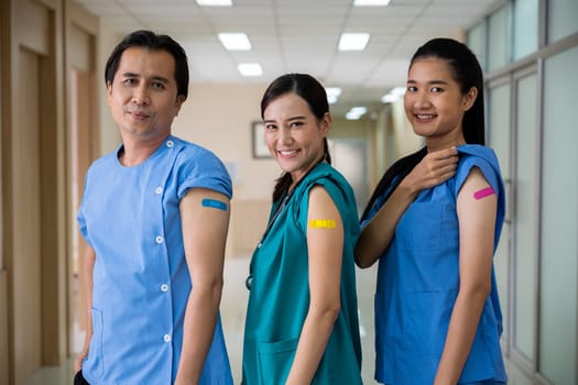 Medical personnel showing to bandage with plaster on arm after getting against Covid-19 vaccine, happy nurse woman and man standing at hospital, Covid-19 vaccination concept
