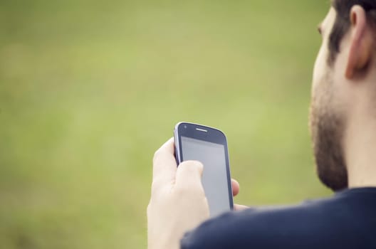 Young man sitting in the park and texting a message