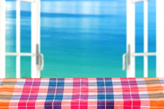 Empty table product. Empty wooden table covered with a colorful checkered tablecloth over abstract blurred ocean background. Space for your food and product display montage.