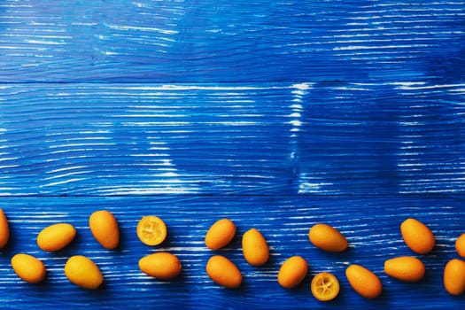 Light blue wooden flat lay table with top view on fresh ripe orange cumquat or kumquat citrus. Full, cut and sliced fruits. Empty copy space for advertisement text. High quality photo