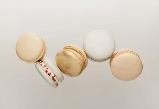 White, yellow, gold macaron cookies flying, falling in motion or levitating. Colorful, sweet small French macaroon cakes. Light beige background. Broken cut, bitten parts, halves. High quality photo