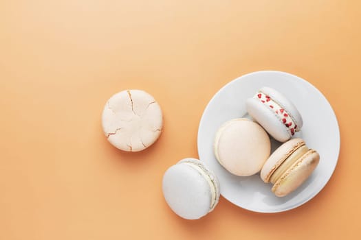 White, yellow, gold macaron cookies. Colorful, sweet small French macaroon cakes. Light yellow background. Broken cut, bitten parts, halves. White plate laying on the table. High quality photo