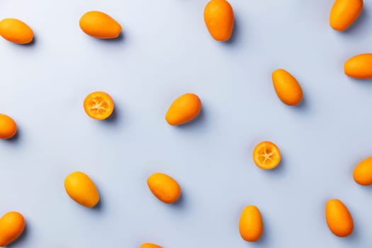 Light blue flat lay with top view on fresh ripe orange cumquat or kumquat citrus. Full, cut and sliced fruits. High quality pattern photo. Healthy eating concept. Vegan or vegetarian eating food