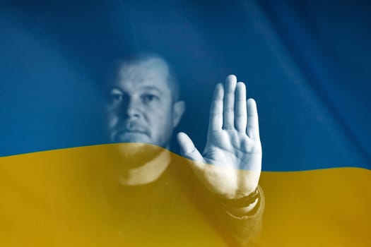 War between Russia and Ukraine. Man with sad sight, showing Stop gesture over Ukraine flag.