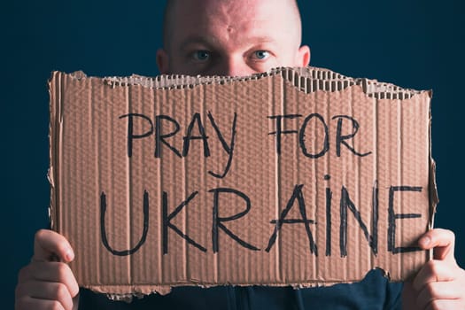 Man holding Pray for Ukraine banner. Concept symbol of help support and no war in the country of Ukraine.