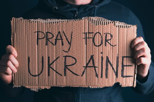 Man holding Pray for Ukraine banner. Concept symbol of help support and no war in the country of Ukraine.