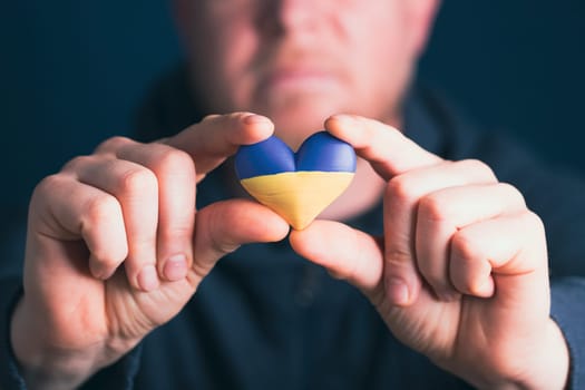 Heart shaped flag of Ukraine in male hands. The concept of solidarity with the citizens of Ukraine.