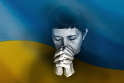 Sad woman with Ukraine flag at background praying. Concept of standing with Ukrainian nation in war with Russia.