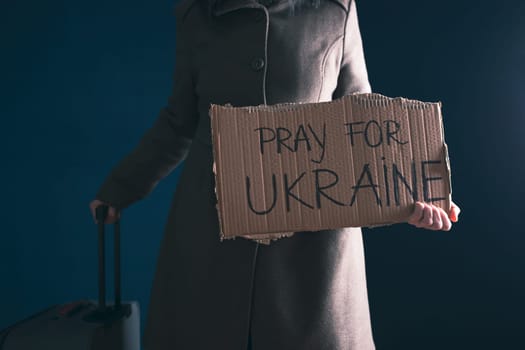 Ukrainian refugee holding placard with Pray for Ukraine text. Evacuation of civilians. Freedom to Ukraine concept.