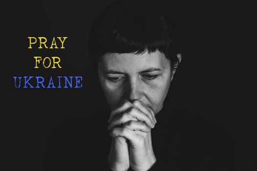 Sad woman with Ukraine flag at background praying. Concept of standing with Ukrainian nation in war with Russia.