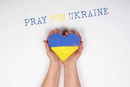 Heart shaped flag of Ukraine in female hands, Pray for Ukraine text.  The concept of solidarity with the citizens of Ukraine.