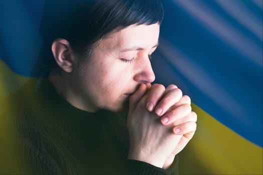 Sad woman with Ukraine flag at background praying. Concept of standing with Ukrainian nation in war with Russia.