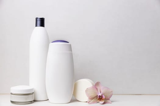 Preparation for spa, home bath procedure. Bathroom accessories, cosmetic on washbasin shelf. Shampoo, shower gel, hair conditioner, soap, cream glass bottle, white soap, orchid flower, copy space