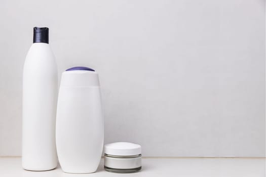 Preparation for hotel spa treatment or home bath procedure. Gray bathroom shelf or table with accessories and cosmetics. Shampoo, shower gel, hair conditioner, soft cream glass bottle with copy space