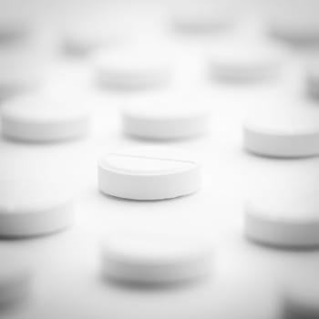 A pile of white pills scattered on a bright white background. Selective focus. Mockup layout, template.