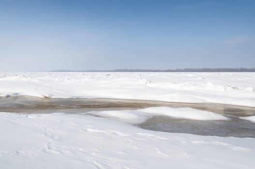 Stunning view of the frozen river covered with chunks of ice and white frosted snow. Snowy desert. The river breaks through the ice.