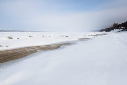 Stunning view of the frozen river covered with chunks of ice and white frosted snow. Snowy desert. The river breaks through the ice.