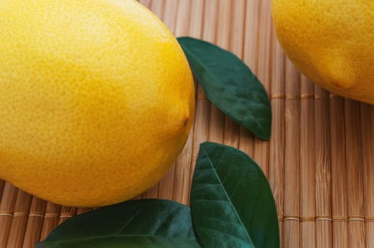 Close-up of large lemons and green leaves on bamboo mat.