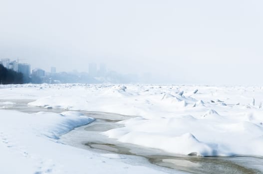 Stunning view of the frozen river covered with chunks of ice and white frosted snow. Snowy desert. The river breaks through the ice.