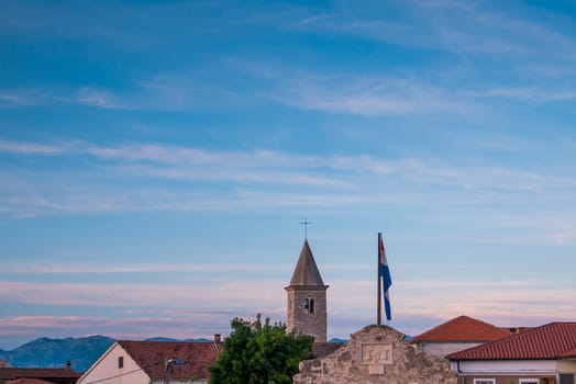 Skyline Of town Nin in Croatia with church tower, red roofs and Croatian flag on a blue sky with little clouds