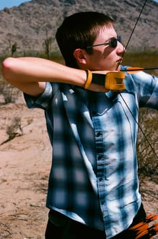 Young man shooting a bow and arrow in the desert