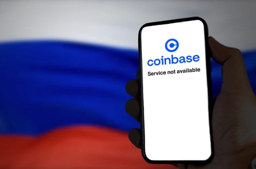 Moscow, RUS, March 2022: Hand holding a phone with the Coinbase app out of service on screen with the Russian flag blurred in the background. In March 2022 Coinbase blocked 25,000 Russian wallets