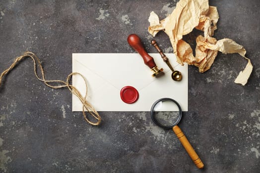 Vintage postal stationery on concrete background. Blank envelope, sealing wax, stamp, spoon, magnifier, crumpled paper and rope.