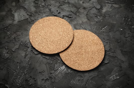 Photo of two blank cork beer coasters on black plaster background.