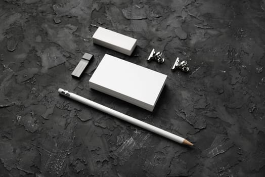 Blank stationery set on black plaster background. Blank business cards, pencil, eraser, usb flash drive and clips.