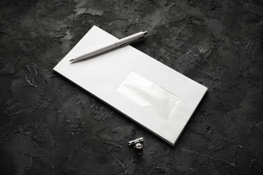 Blank envelope, pen and clip on black plaster background. Branding mock up.