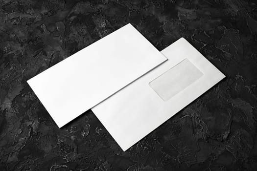 Two blank envelopes on black plaster background. Front and back side. Template for branding identity.