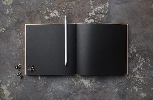 Blank black book and pencil on concrete background. Template for placing your design. Flat lay.