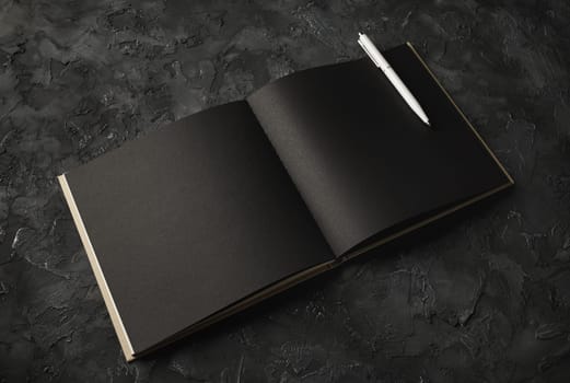 Blank black paper sketchbook and pen on black plaster background. Responsive design template.