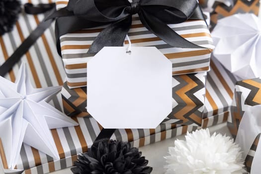 Present with blank gift tag and black bow close up. Gift boxes wrapped in Striped and chevron geometric paper near black and white decor. Christmas, New Year, Birthday, Anniversary label mockup