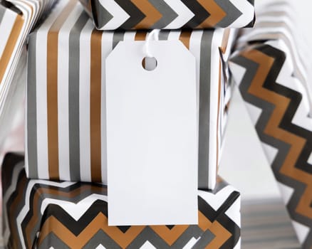 Present with blank vertical gift tag close up. Gift boxes wrapped in Striped and chevron geometric paper. Christmas, New Year, Birthday, Anniversary label mockup