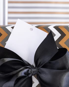 Present with blank square gift tag and black ribbon bow close up. Gift boxes wrapped in Striped and chevron geometric paper. Christmas, New Year, Birthday, Anniversary label mockup