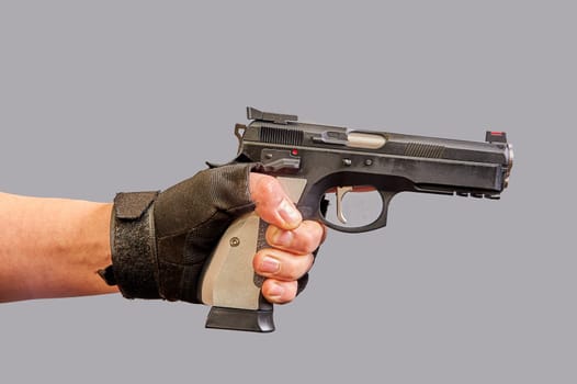 A man's hand holds a black pistol in his hand on a gray background. High quality photo