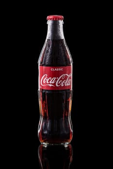 Glass bottle of Coca Cola on a black background with water drops on the surface. High quality photo