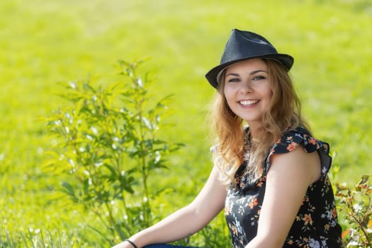 Portrait of smiling attractive  young woman in black straw hat posing outdoors in summer day. Horizontally.