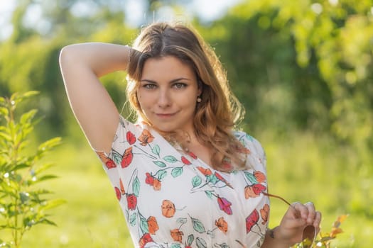 Atractive long hair young woman with both hands in her hair is posing outdoors. Horizontally.