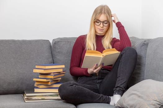 Young woman is sitting on the couch and reading a book. Self education concept.