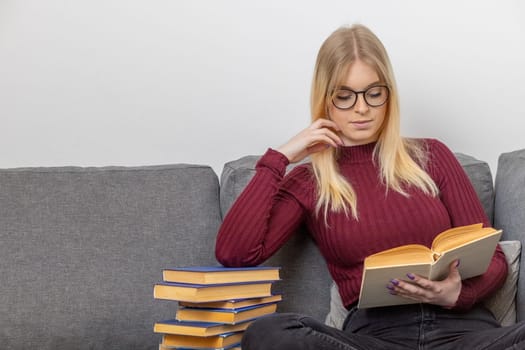 Self education concept. Young woman is leaning on a pile of books and reading a book. Horizontally.