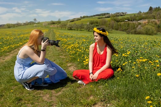 Young girl posing photographing friend sitting in a dandelion meadow.